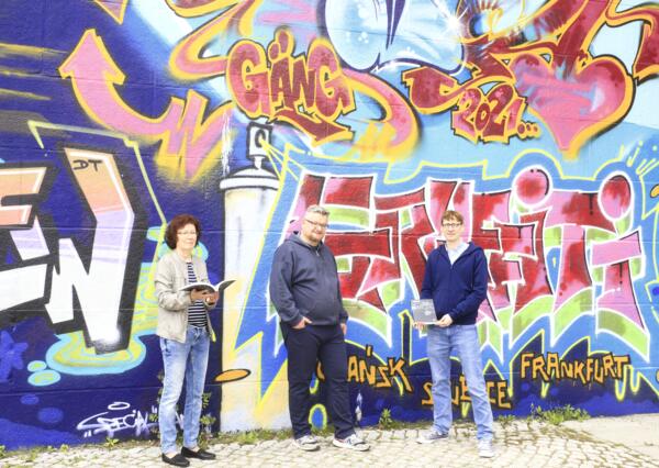 Buchübergabe vor dem Graffiti an der Stadtbrücke mit (v. l. n. r.) Archivbibliothekarin Sigrid Riedel, Jan Augustyniak und Archivleiter Dr. Denny Becker.